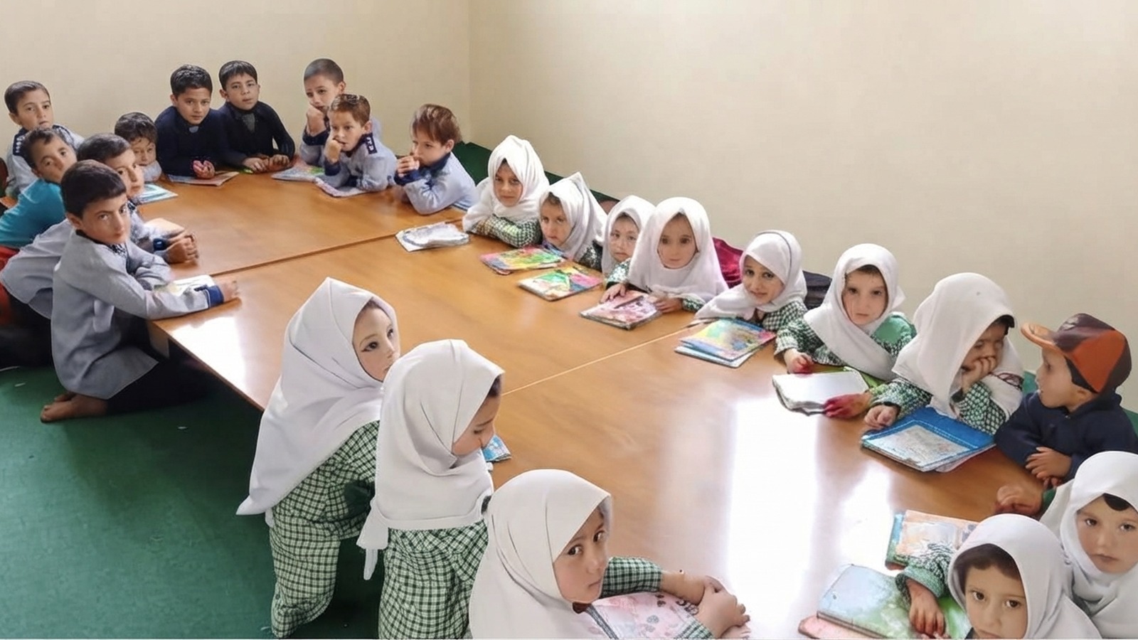 Boys and girls in uniform reading together at low tables in a Khadija Ibrahim Public School classroom