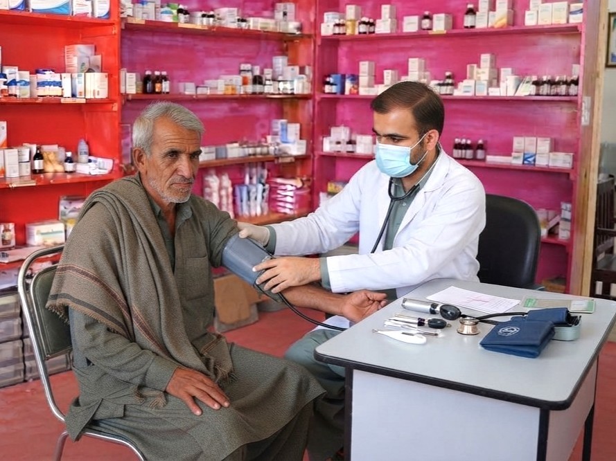 A health worker checking an older patient's blood pressure at a clinic