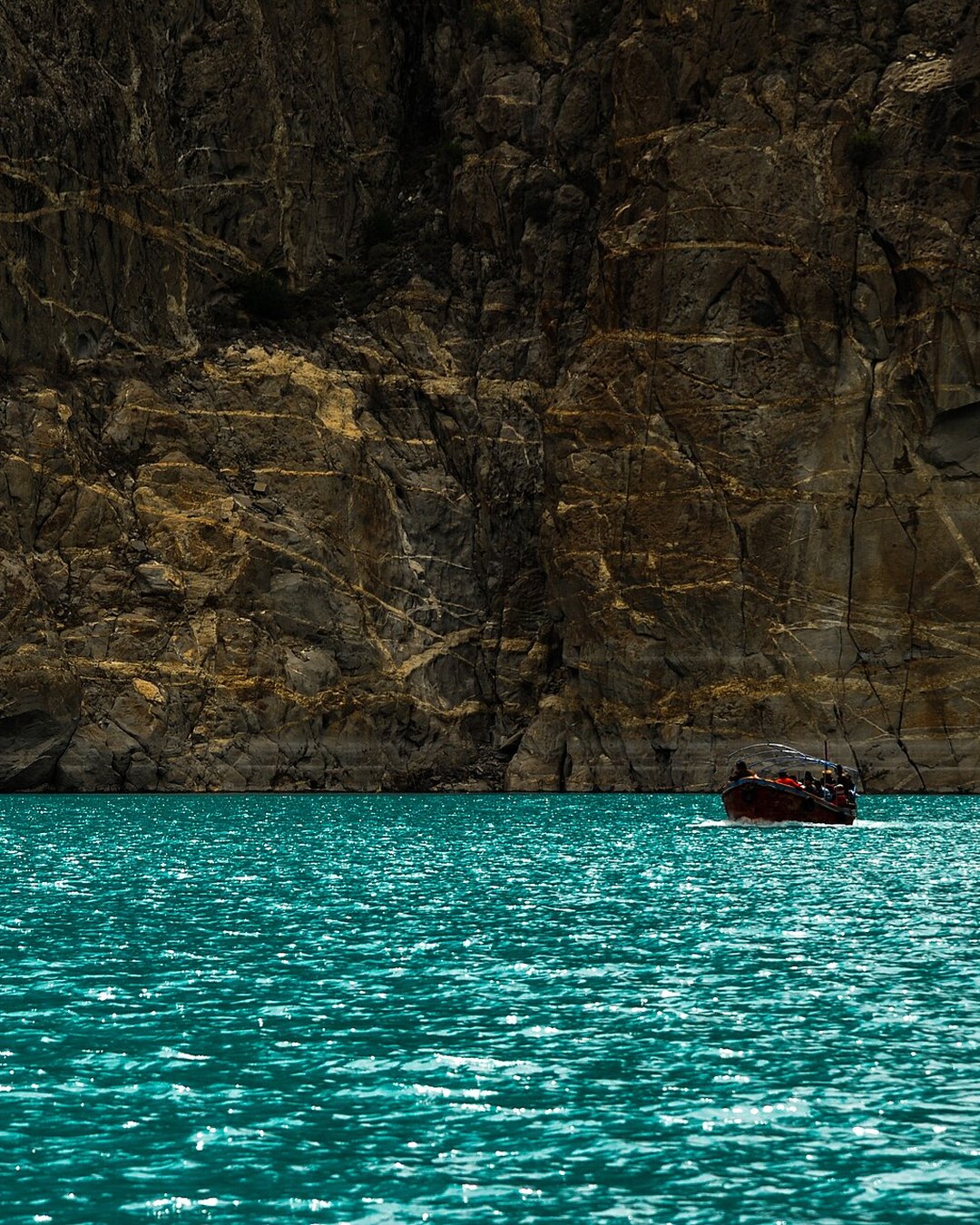 A small boat on the turquoise water of Attabad Lake, framed by a towering rock face
